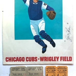 May include: A vintage Chicago Cubs baseball program from Wrigley Field. The program features a cartoon illustration of a catcher in action. The program is dated 1961 and includes tickets for a game. The tickets are for a child's ticket, grandstand seating, and a rain check.