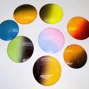 Op de afbeelding: Een verzameling van acht ronde, kleurrijke lenzen in verschillende tinten, waaronder blauw, geel, oranje, roze en groen. Elke lens heeft een gradi&euml;nteffect, dat overgaat van een donkerdere naar een lichtere tint. Op een witte ondergrond.