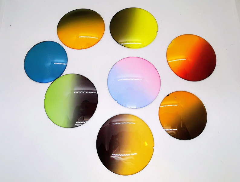 Op de afbeelding: Een verzameling van acht ronde, kleurrijke lenzen in verschillende tinten, waaronder blauw, geel, oranje, roze en groen. Elke lens heeft een gradi&euml;nteffect, dat overgaat van een donkerdere naar een lichtere tint. Op een witte ondergrond.