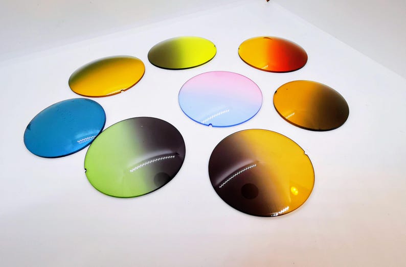 Op de afbeelding: Een assortiment van acht ovale, kleurrijke zonnebrillenglazen. De glazen tonen een verscheidenheid aan kleurenschema's, waaronder geel, blauw, groen, oranje en een roze-blauwe gradi&euml;nt. Elk glas heeft een kleine inkeping aan &eacute;&eacute;n kant.