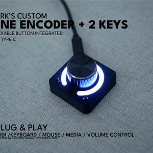 Op de afbeelding: Een zwart vierkant macro-pad met een centrale draaiknop, twee kleine knoppen en een oplichtende witte LED-ring. Het apparaat bevat een USB Type-C poort en kabel. De tekst op de afbeelding luidt: PARK'S CUSTOM ONE ENCODER + 2 KEYS, CLICKABLE BUTTON INTEGRATED, USB TYPE C, PLUG & PLAY, MIDI / KEYBOARD / MOUSE / MEDIA / VOLUME CONTROL.