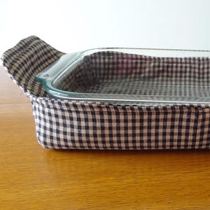 May include: A clear glass baking dish inside a black and white checkered fabric carrier. The carrier has handles on each end. The dish is rectangular and appears empty, ready for baking.
