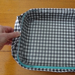 May include: A black and white checkered fabric liner for a glass baking dish. The liner has a smooth, quilted texture and is designed to fit snugly inside the dish.