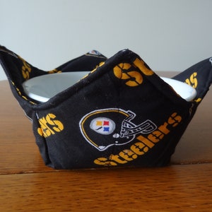 May include: Black and gold fabric bowl cozy with the Pittsburgh Steelers logo. The cozy is designed to hold a bowl and keep it warm.