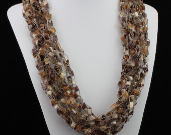 May include: A multi-strand necklace displayed on a white mannequin. The necklace features a woven design with small, square-shaped beads in shades of brown, beige, and gold. The beads are strung together with a dark brown thread, creating a textured look.