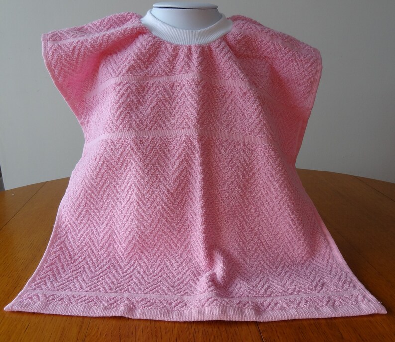 Pullover pink toddler towel bib with white ribbed neck.