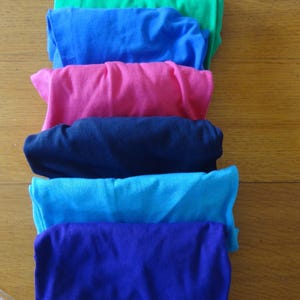 May include: A stack of six folded t-shirts in different colors: green, blue, pink, navy blue, turquoise, and purple.