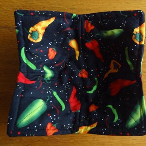 May include: A square, quilted pot holder with a black background. The pot holder is patterned with colorful chili peppers in shades of red, green, and yellow. White dots are scattered across the fabric.