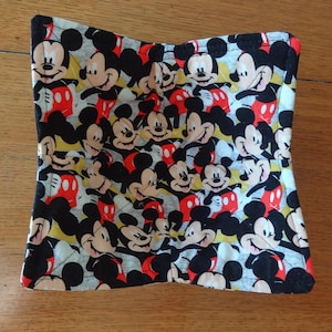 May include: A square, quilted bowl cozy featuring a repeating pattern of Mickey Mouse. The fabric has a light gray background with Mickey's face and body in black, red, yellow, and white. The cozy is designed to hold a bowl.