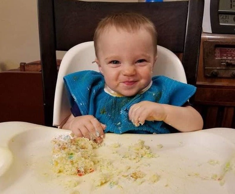 Toddler boy in high chair eating cake and wearing a pullover towel bib.