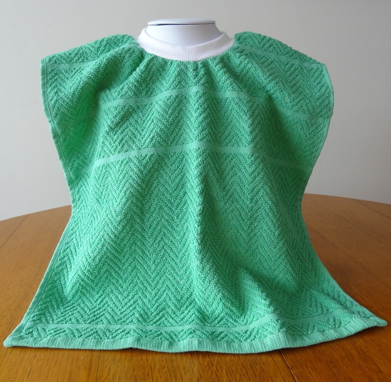 Pullover green toddler towel bib with white ribbed neck.