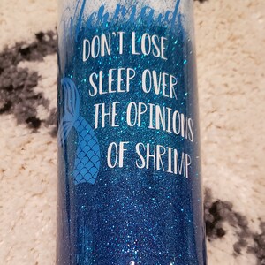 May include: A blue and white glitter tumbler with a mermaid tail and the text "Don't lose sleep over the opinions of shrimp".