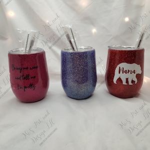 May include: Three stainless steel wine tumblers with glitter finishes. The tumblers are red, purple, and blue. The red tumbler has a white bear with the word "Mama" on it. The purple tumbler has a glitter finish. The red tumbler has the text "Bring me wine and tell me I'm pretty".