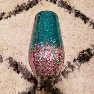 May include: A teal and pink glitter tumbler with a gradient design. The tumbler is made of stainless steel and has a double-walled construction to keep drinks cold or hot.