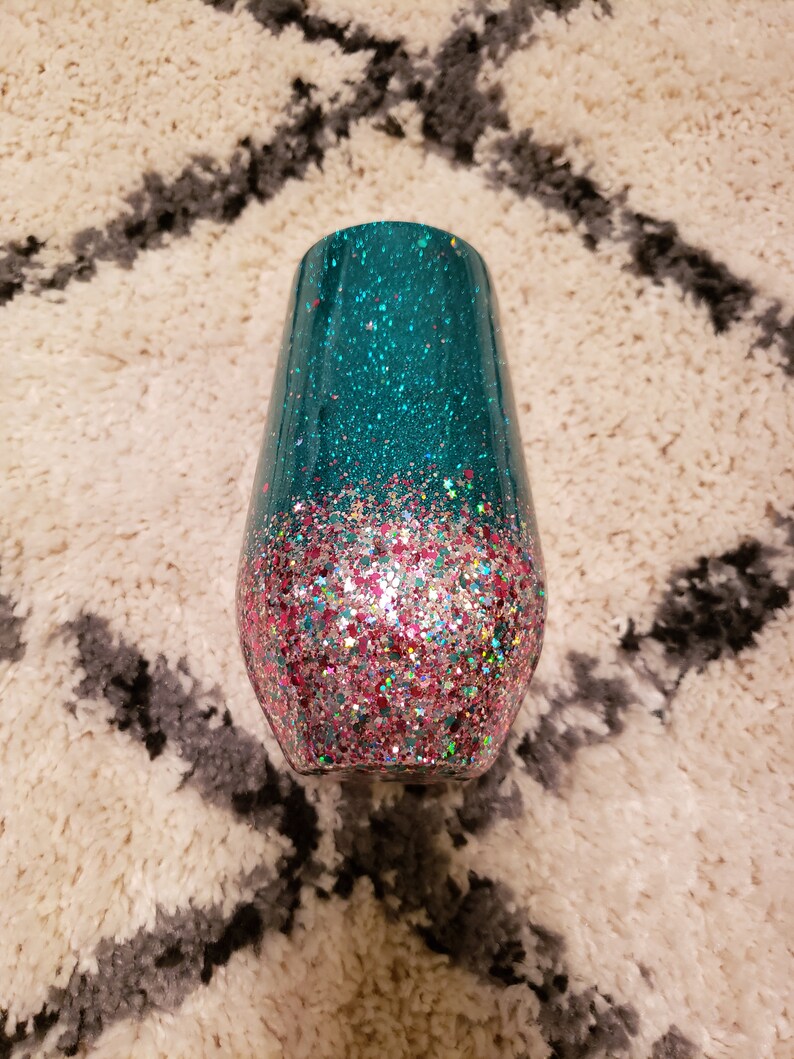 May include: A teal and pink glitter tumbler with a gradient design. The tumbler is made of stainless steel and has a double-walled construction to keep drinks cold or hot.