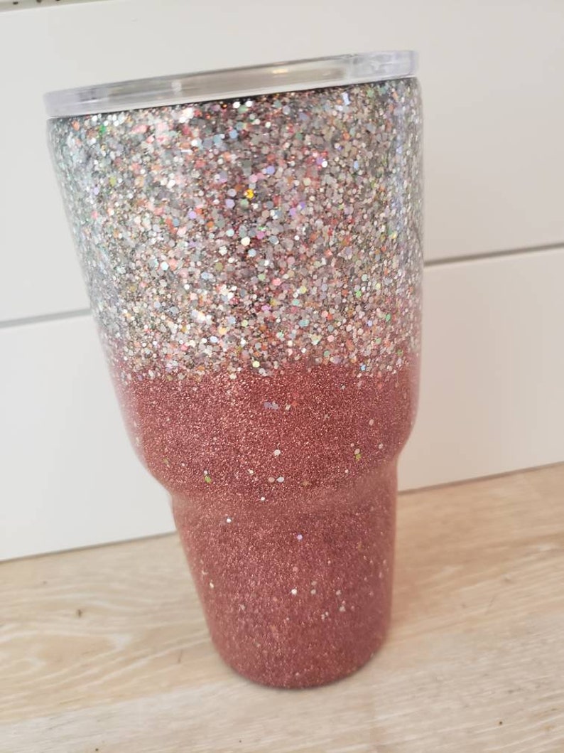 May include: A tall, clear tumbler with a silver glitter top and a rose gold glitter bottom.