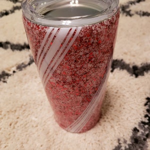 May include: A red and white glitter tumbler with a clear lid. The tumbler has a swirling design of white stripes on a red glitter background.