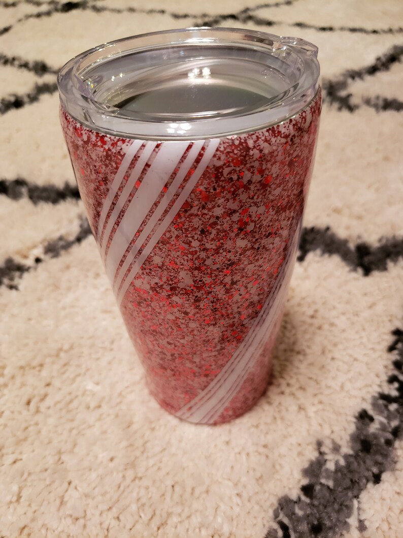 May include: A red and white glitter tumbler with a clear lid. The tumbler has a swirling design of white stripes on a red glitter background.