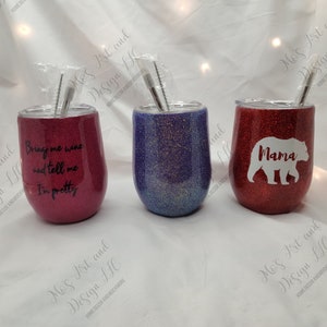 May include: Three stainless steel wine tumblers with glitter finishes. The tumblers are red, purple, and blue. The red tumbler has a white bear with the word "Mama" on it. The purple tumbler has a glitter finish. The red tumbler has the text "Bring me wine and tell me I'm pretty".
