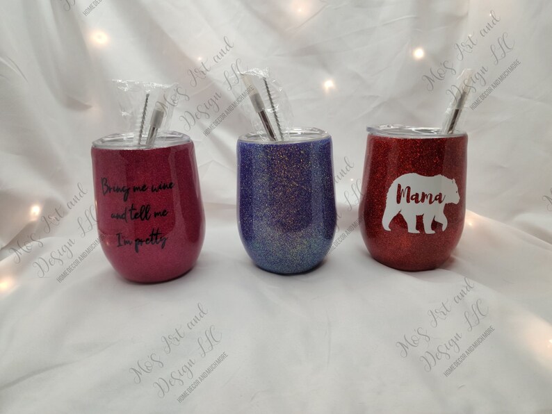 May include: Three stainless steel wine tumblers with glitter finishes. The tumblers are red, purple, and blue. The red tumbler has a white bear with the word "Mama" on it. The purple tumbler has a glitter finish. The red tumbler has the text "Bring me wine and tell me I'm pretty".