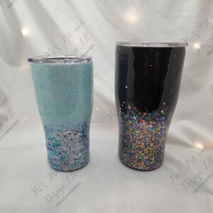 May include: Two stainless steel tumblers with glitter accents. One tumbler is black with multi-colored glitter, and the other is light blue with white and blue glitter.