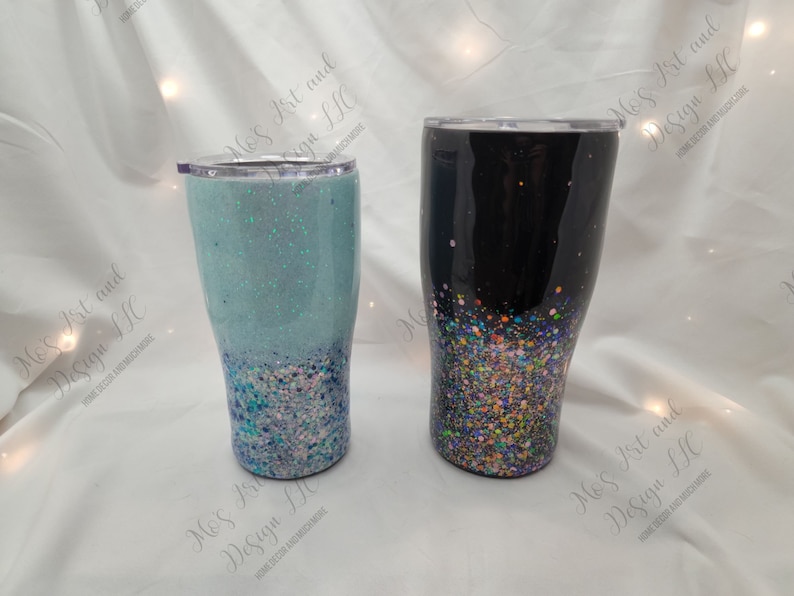 May include: Two stainless steel tumblers with glitter accents. One tumbler is black with multi-colored glitter, and the other is light blue with white and blue glitter.