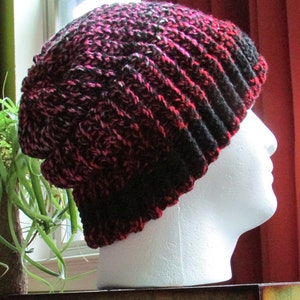 以下が含まれることがあります： ゆったりとしたフィットの黒とピンクのニットビーニー。白いマネキンヘッドにディスプレイされています。