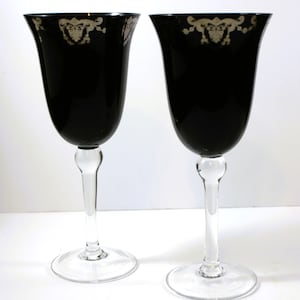 Peut inclure: Deux verres à vin noirs avec une bordure argentée et des tiges transparentes. Les verres sont sur un fond blanc.