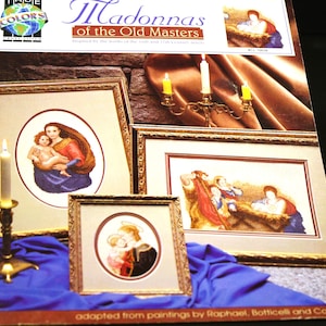 May include: A cross-stitch pattern book featuring Madonnas of the Old Masters. The cover shows four framed cross-stitch patterns inspired by paintings by Raphael, Botticelli, and Correggio. The book is titled "Madonnas of the Old Masters" and includes the text "Inspired by the works of the 14th and 15th century artists."