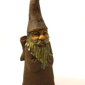 May include: A ceramic gnome figurine with a brown hat, a long white beard, and a brown robe. The gnome is carrying a small sack on its back.