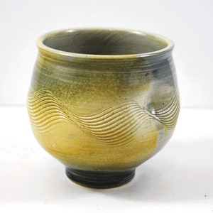 May include: A handcrafted ceramic bowl with a unique wave pattern. The bowl features a blend of yellow, green, and blue hues. The base is dark, and the rim is slightly flared. This decorative bowl is suitable for serving or display.