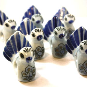 May include: A collection of ceramic bird figurines. Each bird has a white body with blue and white striped wings. The birds have black and white striped heads and are decorated with a floral design in shades of blue and brown.