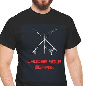 May include: Black t-shirt with a navy blue square featuring white crossed fishing rods and the red text "CHOOSE YOUR WEAPON." The shirt is made of a soft material.