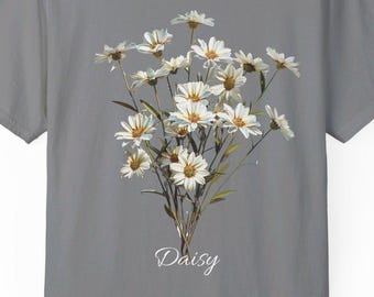 Op de afbeelding: Een grijs T-shirt met een witte madeliefjesboeket-afbeelding en het woord "Daisy" gedrukt onder de afbeelding.