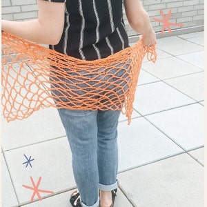 May include: A woman wearing a black and white striped shirt and blue jeans is holding a bright orange crochet net scarf.