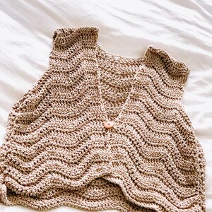 Pu&ograve; includere: Un gilet senza maniche all'uncinetto color beige caratterizzato da un motivo a punti ondulati a chevron su tutta la superficie. Il capo presenta un profondo scollo a V ed &egrave; chiuso al centro davanti da un piccolo bottone in legno chiaro.