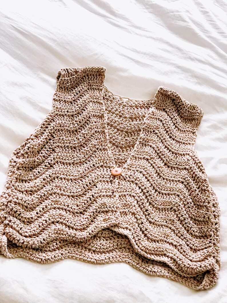 Pu&ograve; includere: Un gilet senza maniche all'uncinetto color beige caratterizzato da un motivo a punti ondulati a chevron su tutta la superficie. Il capo presenta un profondo scollo a V ed &egrave; chiuso al centro davanti da un piccolo bottone in legno chiaro.