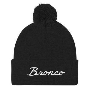 Peut inclure: Bonnet en tricot noir avec un logo "Bronco" brodé en blanc et un pompon noir sur le dessus.