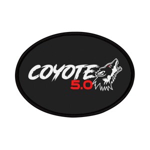 May include: An oval-shaped black embroidered patch featuring the white text COYOTE in a stylized font, the red text 5.0 below it, and a white graphic illustration of a howling coyote head with red accents on the right side.