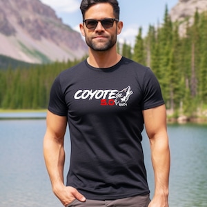 May include: A black t-shirt with a white graphic of a wolf howling and the text "Coyote 5.0" in red and white.