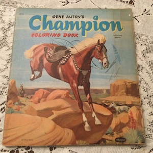 Pode incluir: Capa vintage do "Livro de colorir Champion de Gene Autry" com um cavalo marrom saltando sobre rochas. O título é em azul e vermelho, com o texto "Edição Autorizada". O fundo mostra uma paisagem desértica.