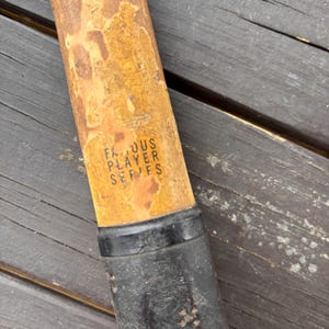 May include: Close-up of a wooden tennis racket handle with a black grip. The handle is labeled "Famous Player Series".