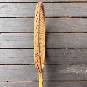 May include: A vintage wooden tennis racket with a brown leather grip and a natural wood frame. The racket has a worn, distressed look, suggesting it has been used for many years.
