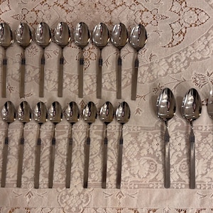 Può includere: Un set di 19 cucchiai argentati e una forchetta, disposti su una tovaglia di pizzo bianco. I cucchiai hanno una ciotola arrotondata e un manico lungo e sottile.