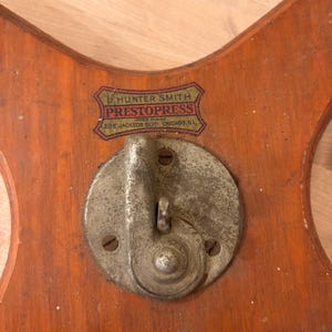May include: A wooden base with a metal crank and a label that reads "U. Hunter Smith PrestoPress Automatic Clothes Press 20 E. Jackson Blvd. Chicago, Ill."