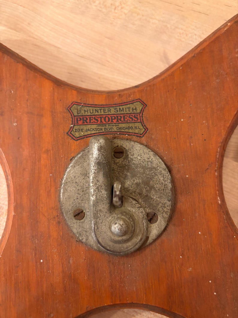 May include: A wooden base with a metal crank and a label that reads "U. Hunter Smith PrestoPress Automatic Clothes Press 20 E. Jackson Blvd. Chicago, Ill."