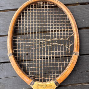May include: A vintage wooden tennis racket with a worn stringed frame and a faded label that reads "International Model" with a picture of a man.