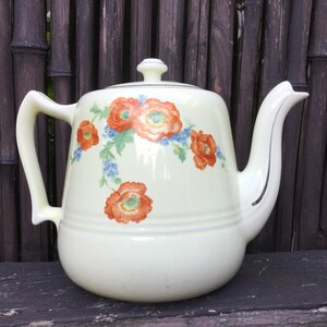 May include: Cream-colored ceramic teapot with a lid, handle, and spout. The teapot is decorated with orange and red floral patterns and blue accents. The teapot has a capacity of approximately 1.5 liters.