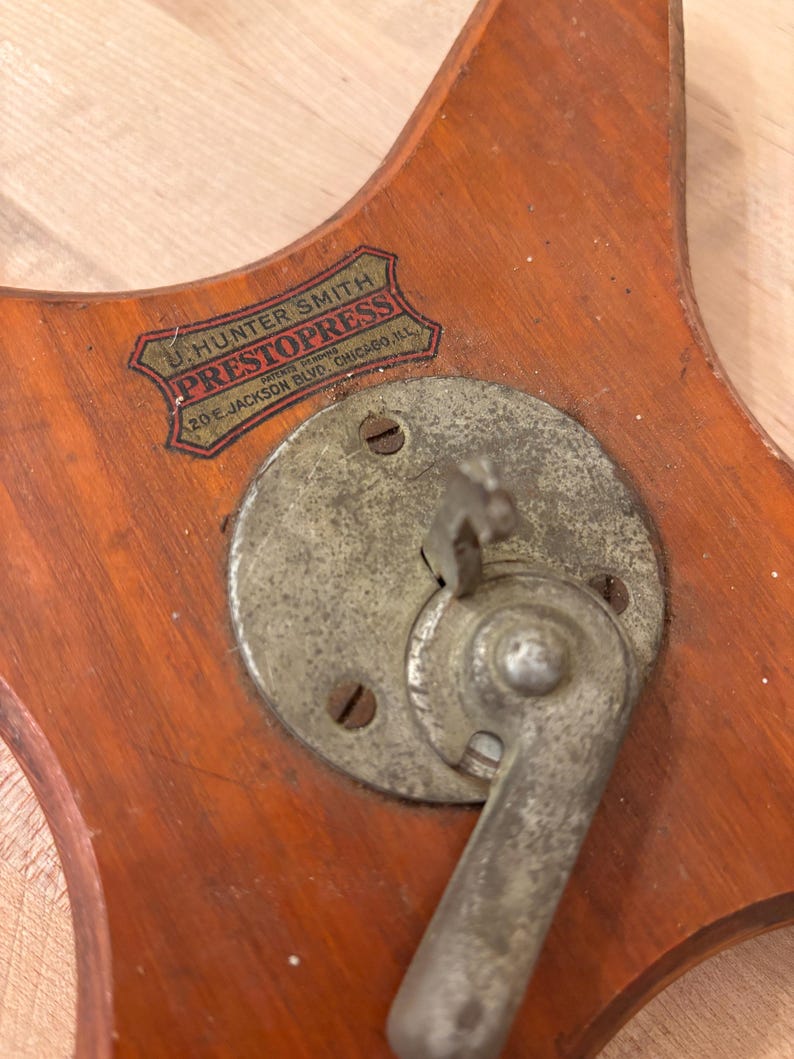May include: A vintage wooden base with a metal lever and a label that reads "J. Hunter Smith, Patented, PrestoPress, 20 E. Jackson Blvd., Chicago, Ill."