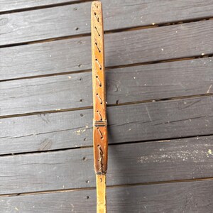 May include: A wooden tennis racket with a brown leather grip and stitching. The racket is made of wood and has a natural finish.